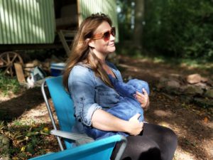 Mom with brown hair and sunglasses sitting on chair outside nursing baby
