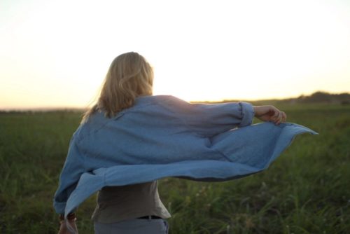 woman walking through field wearing denim shirt